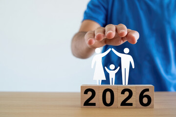 Hand offers protection over small family figures resting on a 2026 wooden block for planning.