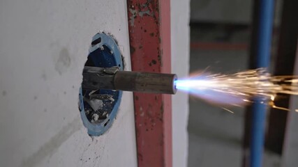 A close-up shot of a construction scene shows a flame torch creating sparks in a wall opening - Powered by Adobe