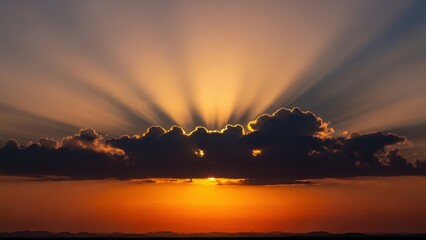 Magnificent sunset with radiant sunrays emerging behind silhouetted clouds over a tranquil horizon