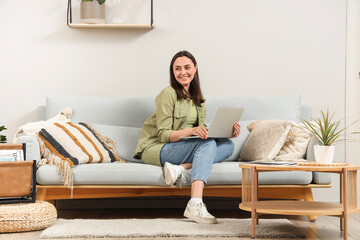 Young woman using laptop on grey sofa near light wall at home