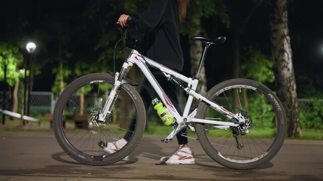Quiet Evening Bicycle Maintenance, Calm Evening Atmosphere Showing Woman Fixing Bicycle Under Lamp, Peaceful Nighttime Setting With Woman Preparing Her Bicycle For Ride Under Gentle Illumination