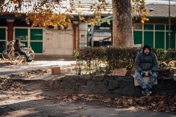 Homeless man needing food sitting on street in autumn