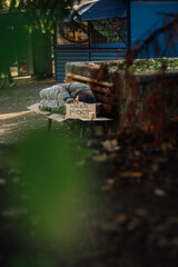 Homeless person sleeping on bench with need food sign