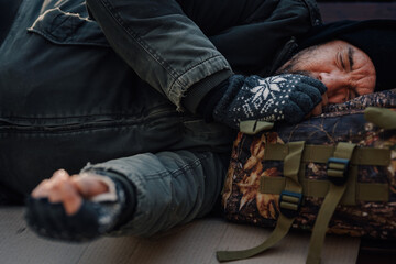 Homeless man sleeping on cold street, urban poverty concept