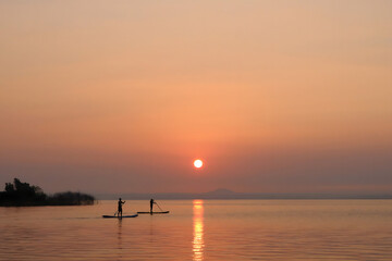 Two People Paddleboarding on Calm Lake at Sunrise