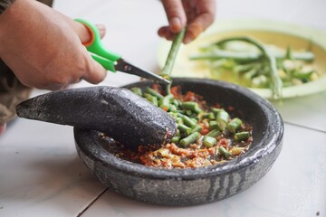 Cutting long beans with scissors. Making traditional Indonesian rujak with green beans using a mortar and pestle, mixed with spicy chili sauce.