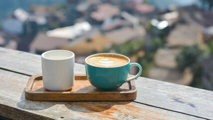 Hot cappuccino in a blue cup, served with hot water, on a wooden table and blurry nature background.