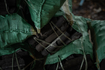 Charcoal bundles wrapped in green mesh bags, stacked for storage. texture and color contrast create...