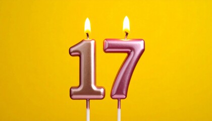 Metallic pink and gold number 17 birthday candle with flame, set against bright yellow background.