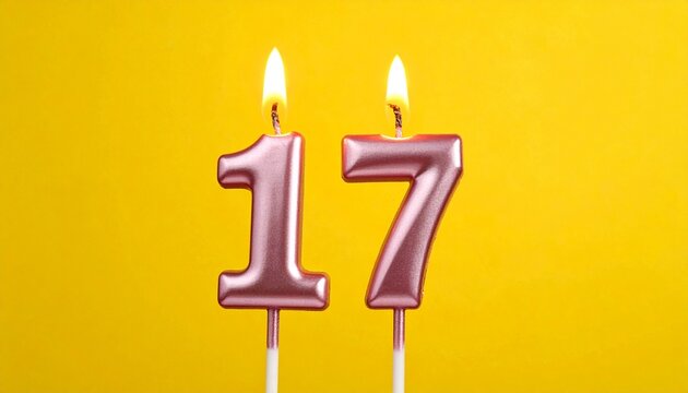 Metallic pink and gold number 17 birthday candle with flame, set against bright yellow background.