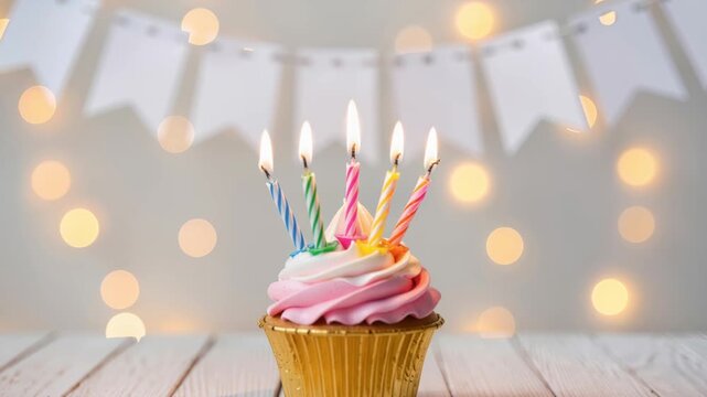 A cupcake with pink and white cream frosting and six burning candles stands on a wooden surface. Glowing bokeh lights and festive flags behind. Sweet party dessert.