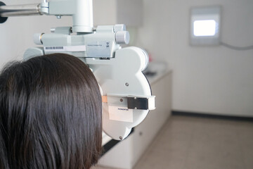 6-year-old Thai girl getting an eye exam with a phoropter at an optical clinic. Pediatric optometry and vision care concept.