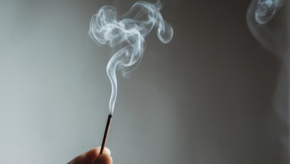 A close-up of a burning incense stick, emitting wispy smoke