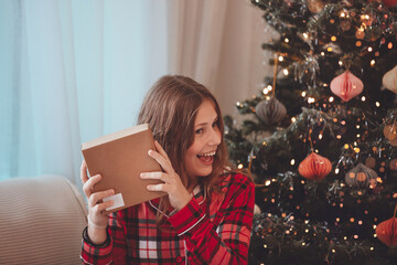 Young Woman Unwrapping Christmas Gift By Decorated Tree