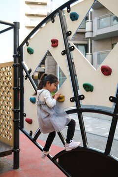 Young Japanese girl playing on playground climbing wall