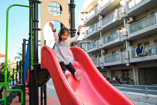 Japanese little girl happily sliding down playground slide