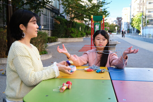 Japanese mother and daughter learning string game in park