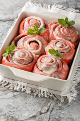 Close-up of pink cinnamon rolls with white icing in a baking dish on a table. Vertical