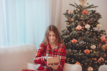 Smiling Girl In Pajamas Beside Christmas Decorated Tree
