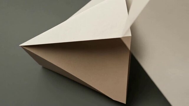 Dynamic interplay of light and shadow on a captivating abstract paper sculpture, revealing intricate geometric folds and a minimalist design aesthetic against a clean, neutral background