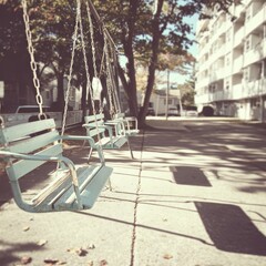 Three empty swings hang silently in a quiet residential area, casting long shadows on the pavement