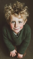 A charming toddler with curly blond hair smiles sweetly while wearing a green sweater