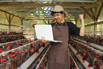 Modern Farmer Celebrating Poultry Farm Success on Laptop in Chicken Coop © Gatot