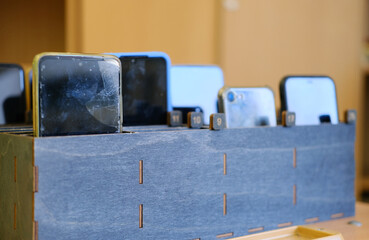 Collection of students' cell phones stored in a wooden box, showcasing various devices with screens facing forward, emphasizing the concept of restricted phone usage in educational settings