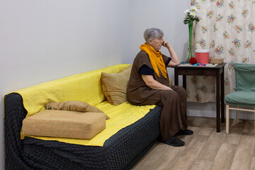 Elderly woman sitting alone on a sofa, looking sad and thoughtful. Concept of loneliness in older age. Mental health awareness for senior citizens.