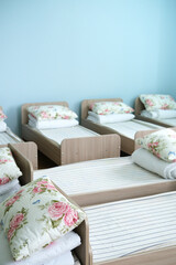 Children's beds arranged in a cozy preschool room with floral pillows and soft linens, creating a serene sleep environment for young children with copy space