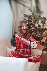 Young Woman Unwrapping Christmas Gift By Decorated Tree