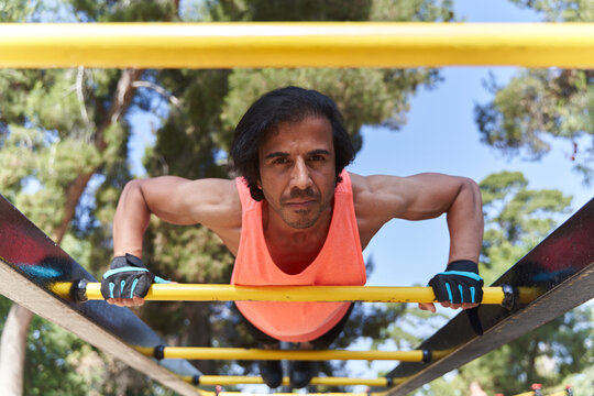 Determined male athlete performing push ups on parallel bars in outdoor gym