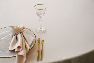 Wedding banquet table setting with white tablecloth, gold-rimmed plate, folded napkin, glass, and cutlery arranged neatly with copy space for design
