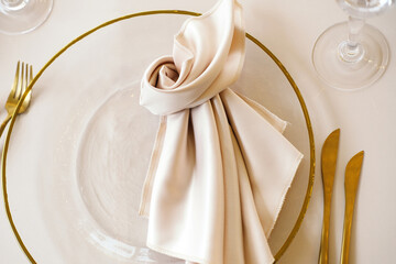 Beautifully arranged table setting showcases a clear glass plate with golden rim, cream napkin, golden cutlery, and crystal glasses, ideal for elegant dining experiences