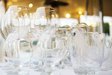 Glassware collection including wine glasses, tumblers, and a pitcher arranged on a table with blurred background lights and soft bokeh effect during an outdoor event