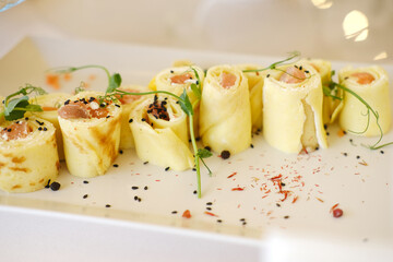 Gourmet sushi rolls made with delicate crepes, filled with fresh fish and garnished with microgreens, served elegantly on a white plate, showcasing culinary artistry and presentation