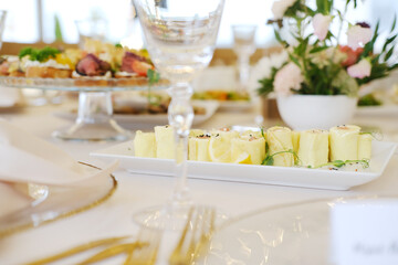 Platter of yellow food items with lemon slices on white rectangular dish in foreground, crystal glassware and floral arrangement in background on dining table