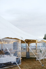 Large outdoor event tent with transparent sides, illuminated by string lights, set on grassy field, creating a cozy atmosphere for gatherings and celebrations