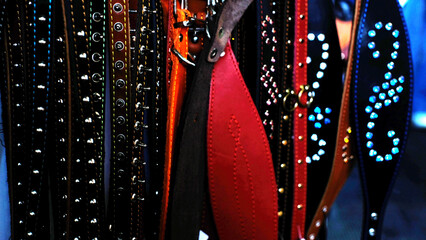 Animal collars in various colors and materials displayed on rack with studs and embellishments, including black, brown, red, and blue collars hanging side by side in close proximity