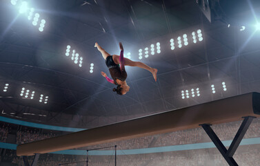 A gymnast performs a difficult trick on a balance beam.