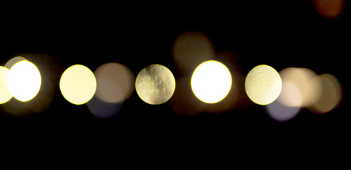 Defocused night lights create soft circular bokeh shapes on dark background. Warm glow and abstract