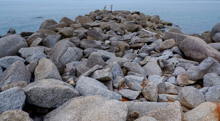 A rocky breakwater made of large granite stones extending into a calm tropical sea, creating a strong leading line and peaceful coastal atmosphere.