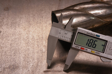 Digital caliper measuring metal pipe diameter on metal sheet on wooden workbench table background.