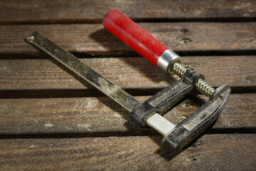 Top view of metal F clamp with red handle on wooden workbench table background.
