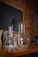 Glass laboratory flasks standing on wooden desk table in school room interior with brick wall background.