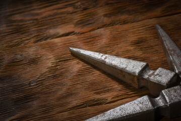Forged metal spike elements arranged in corner composition on dark wooden plank workbench table background with empty copy space.