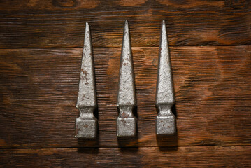 Forged metal spike elements arranged in corner composition on dark wooden plank workbench table background with empty copy space.