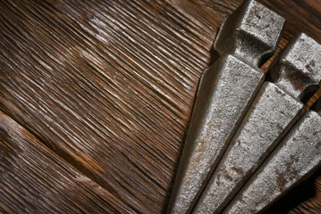 Forged metal spike elements arranged in corner composition on dark wooden plank workbench table background with empty copy space.