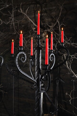 Forged wrought iron floor candelabras with twisted columns and lit red candles in dark medieval castle stronghold interior.