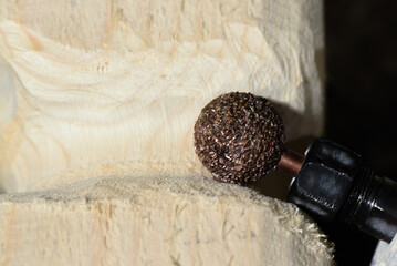 Electric straight grinder with abrasive grinding stone carving wooden surface on workshop close up background.